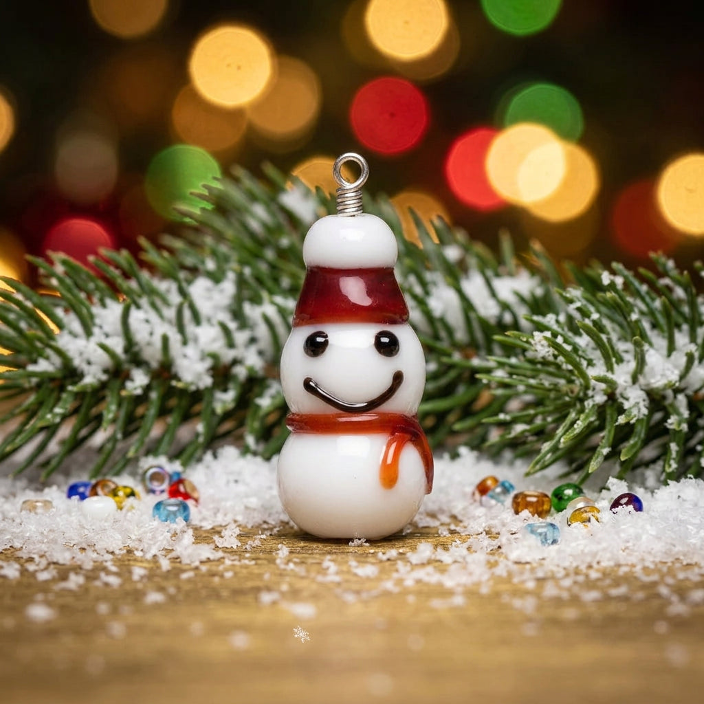 A small glossy snowman figurine or charm with a white body, dark eyes, a red hat, and an orange-brown scarf, shown on a plain white background.