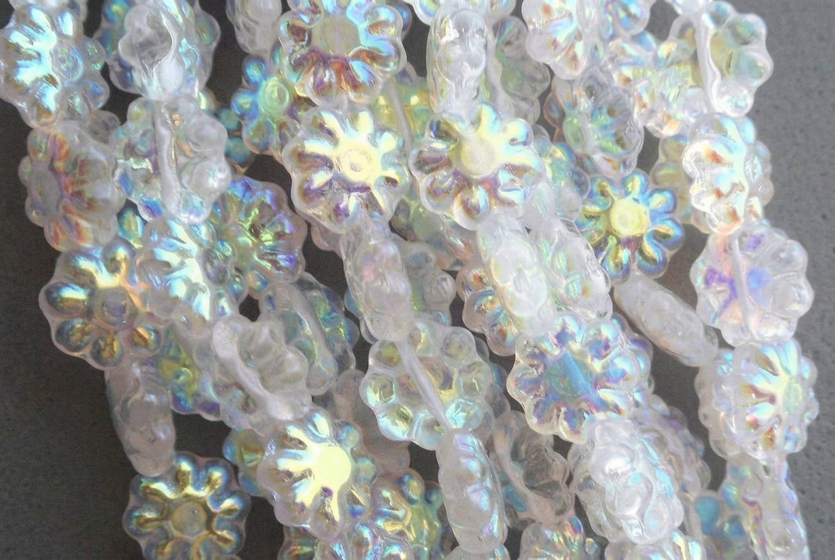 Close-up of iridescent flower-shaped beads with a milky white base and rainbow reflections, overlapping on a dark background.