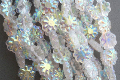 Close-up of iridescent flower-shaped beads with a milky white base and rainbow reflections, overlapping on a dark background.