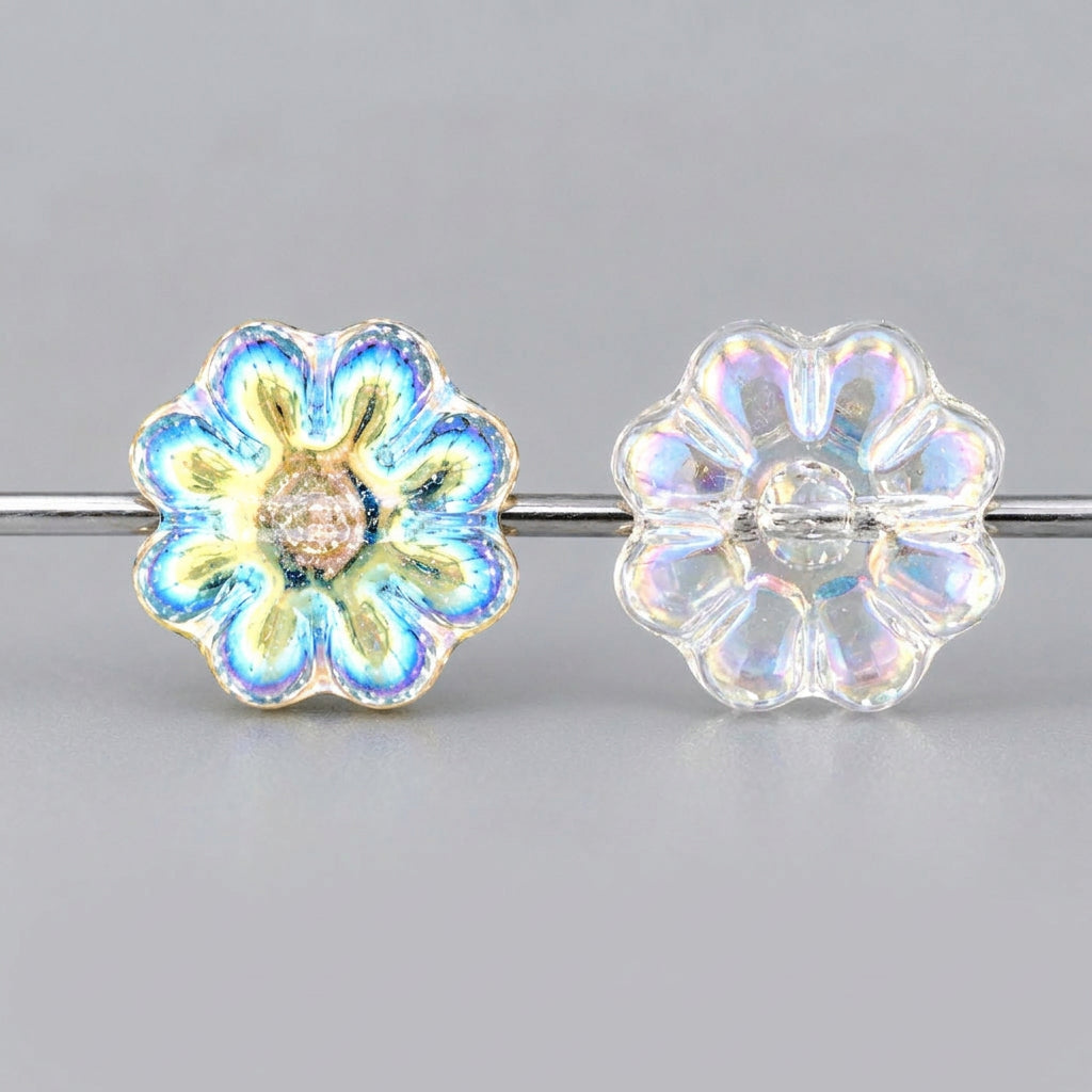 Three decorative flower-shaped beads strung on a black cord, featuring iridescent light blue, white, and clear qualities on a textured gray-green background.