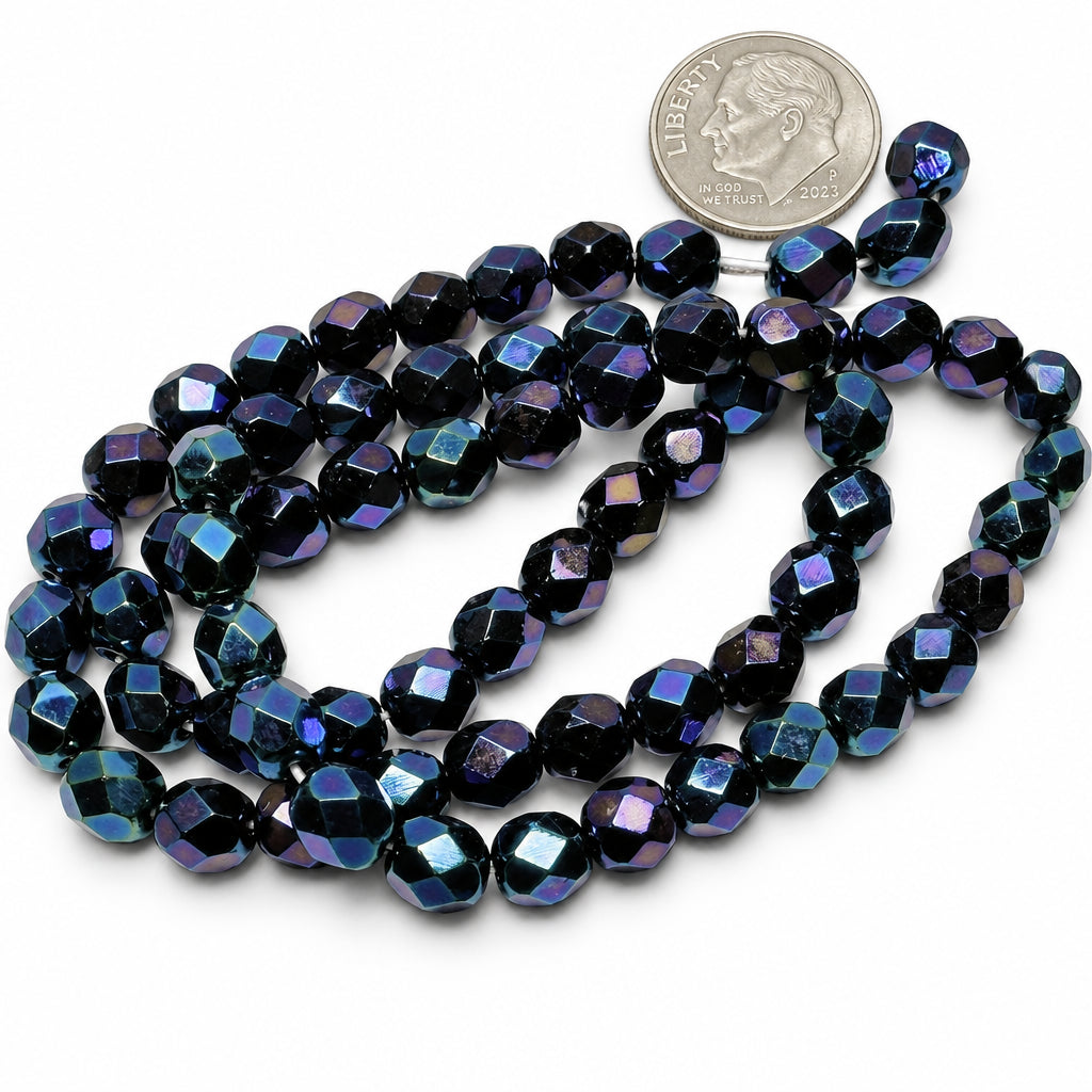 A strand of faceted dark blue and purple beads with an iridescent finish, shown next to a US quarter coin for scale on a white background.
