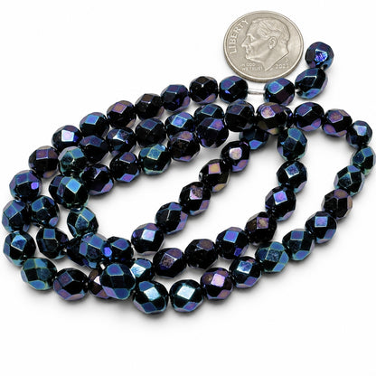 A strand of faceted dark blue and purple beads with an iridescent finish, shown next to a US quarter coin for scale on a white background.