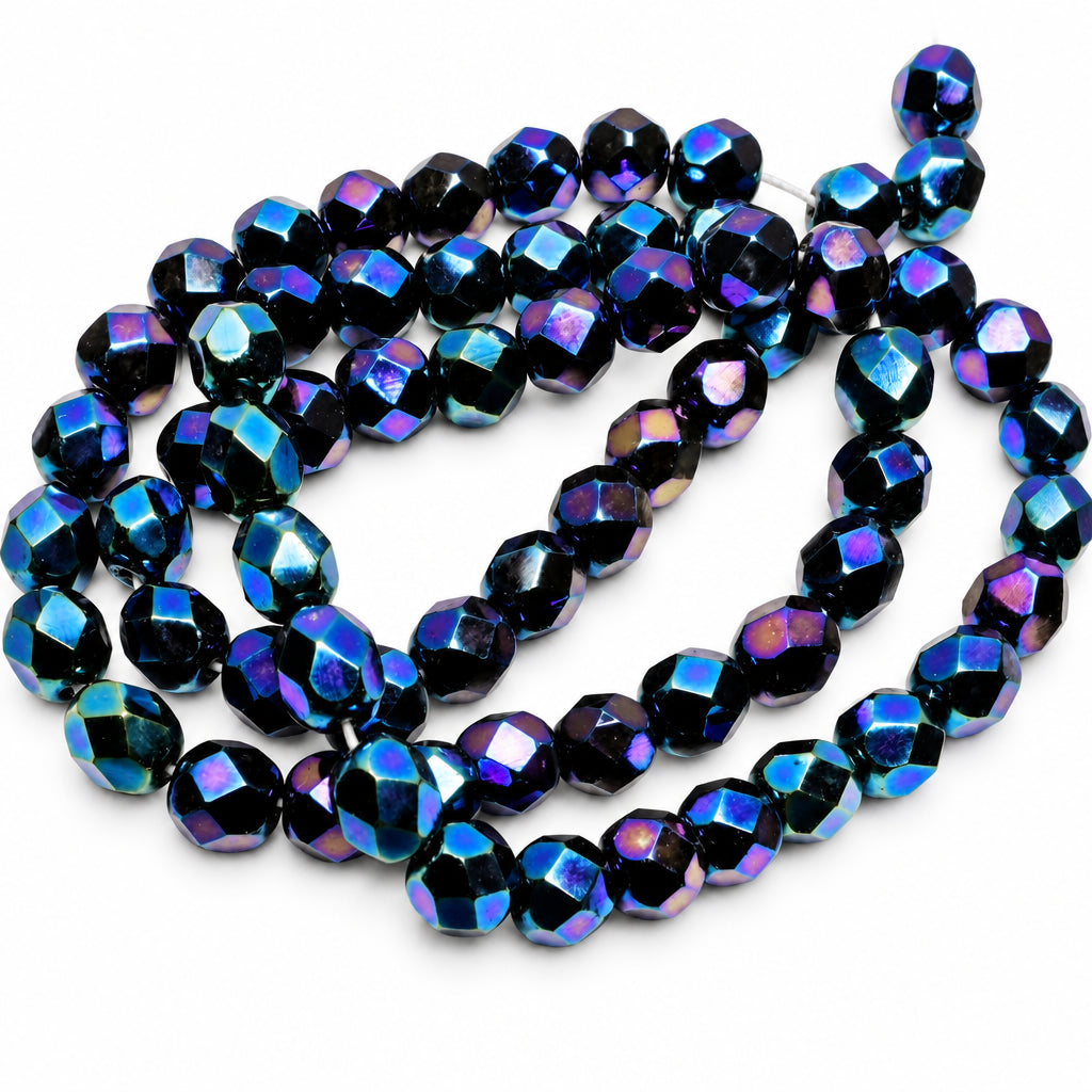 Faceted round beads with an iridescent dark blue, purple, and black finish, arranged in a loose coil on a light gray background.