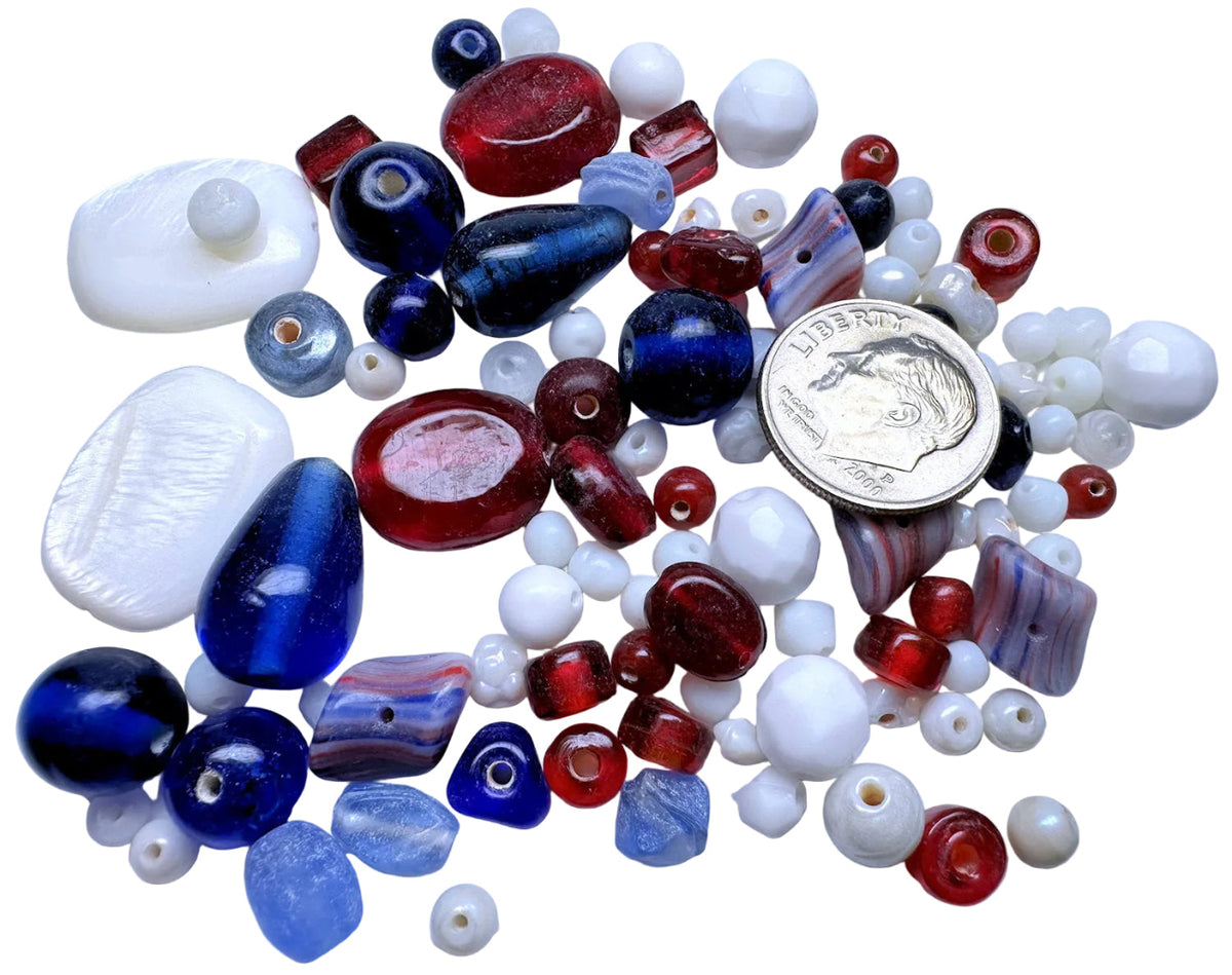 A collection of assorted glass beads in red, blue, white, and purple marbled colors, displayed on a white background with a US dime for scale.