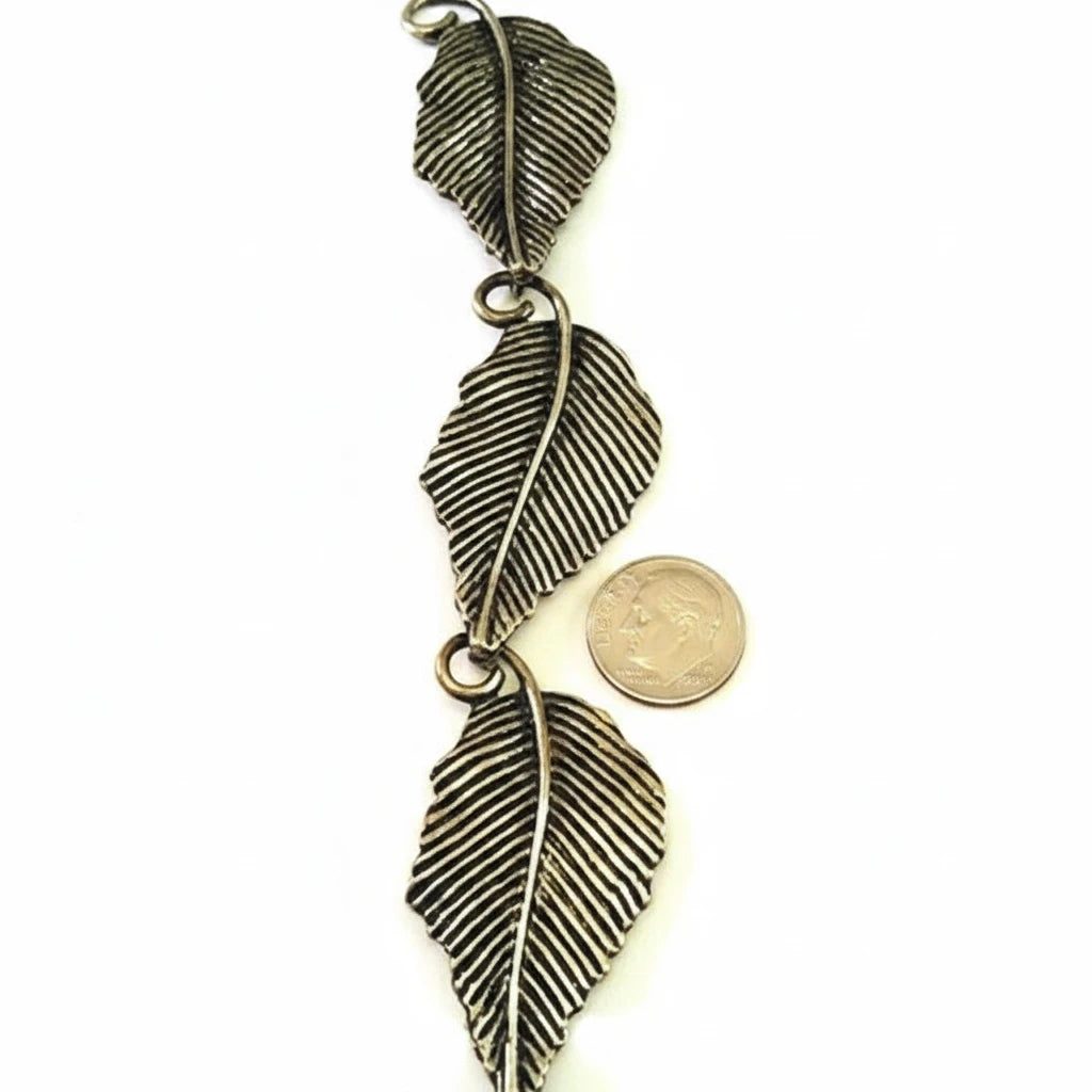 Three antique bronze leaf-shaped charms with detailed textured veins, shown vertically next to a US quarter coin for scale on a light background.