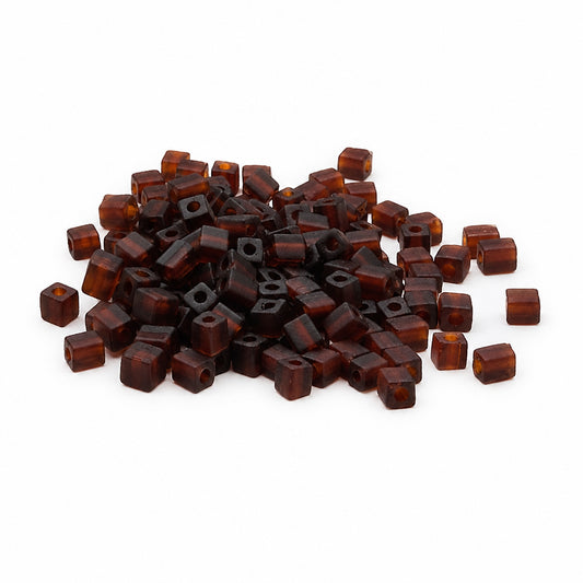 A pile of small translucent square seed beads in a dark amber-brown color, scattered on a plain white background.