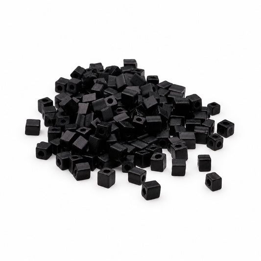 A pile of small matte black square beads with central holes, scattered on a plain white background.