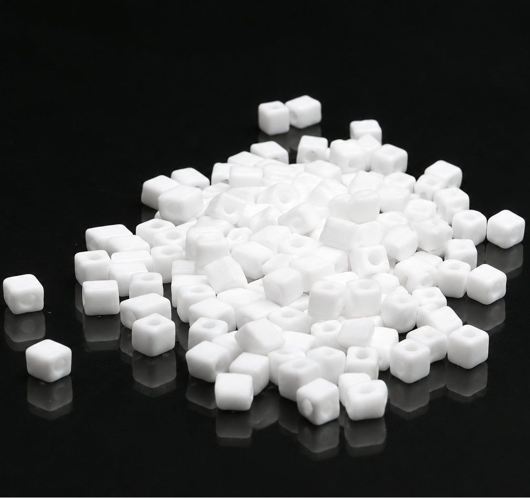 White square bead charms with hollow centers scattered on a reflective black surface.