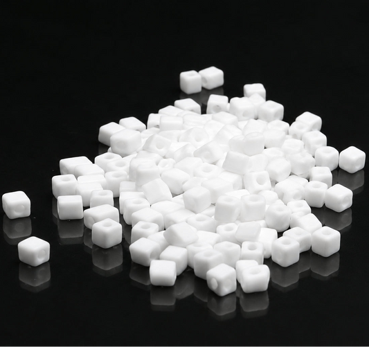 White square bead charms with hollow centers scattered on a reflective black surface.