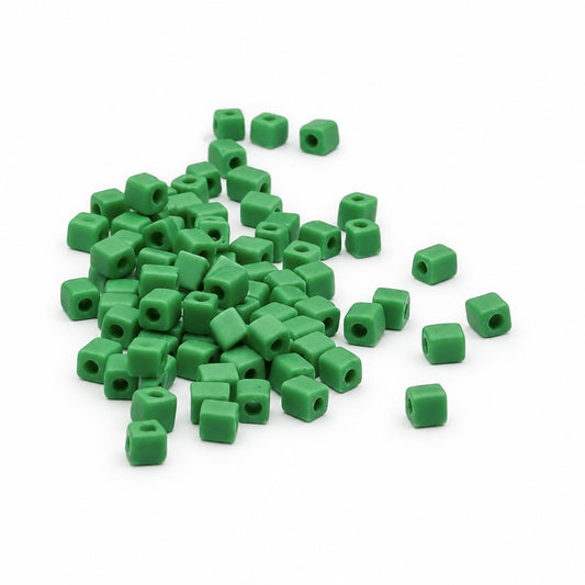 Green square-shaped seed beads with a single center hole, scattered on a plain white background.