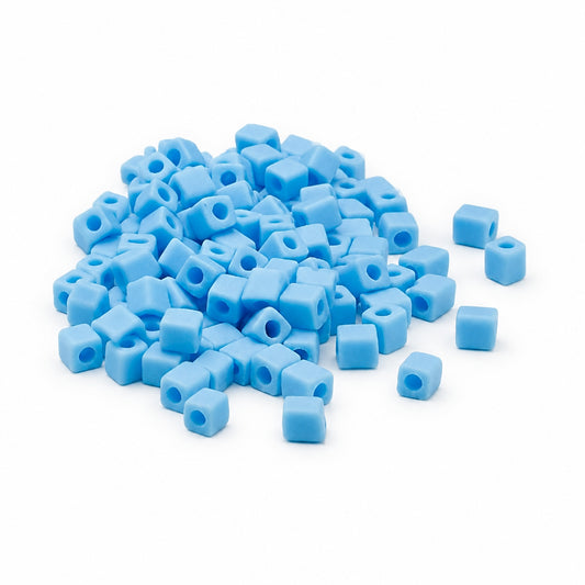 A pile of light blue cube-shaped seed beads with center holes, scattered on a plain white background.