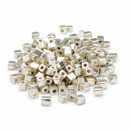 A pile of small metallic silver cube-shaped beads with central holes, scattered on a plain white background.