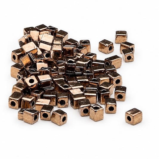 A pile of small metallic cube-shaped beads with holes, shown on a plain white background.