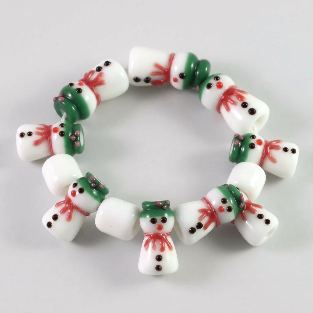 Close-up of a string of festive glass beads shaped like snowmen, featuring white bodies, green hats and scarves, red accents, and black facial details.
