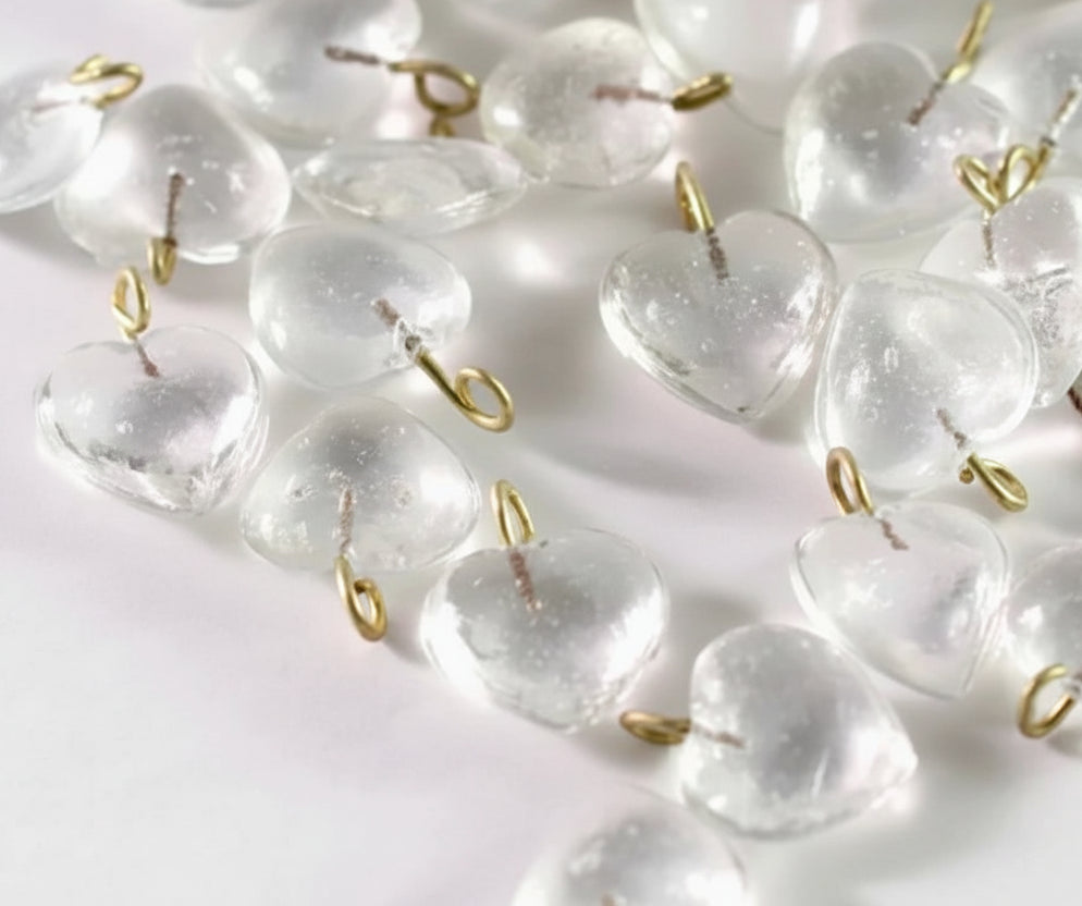 Clear heart-shaped glass beads with small gold metal loops, scattered on a white surface with a coin for scale.