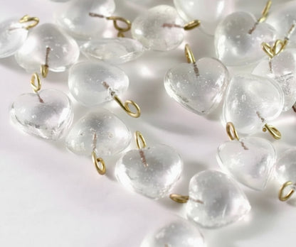 Clear heart-shaped glass beads with small gold metal loops, scattered on a white surface with a coin for scale.