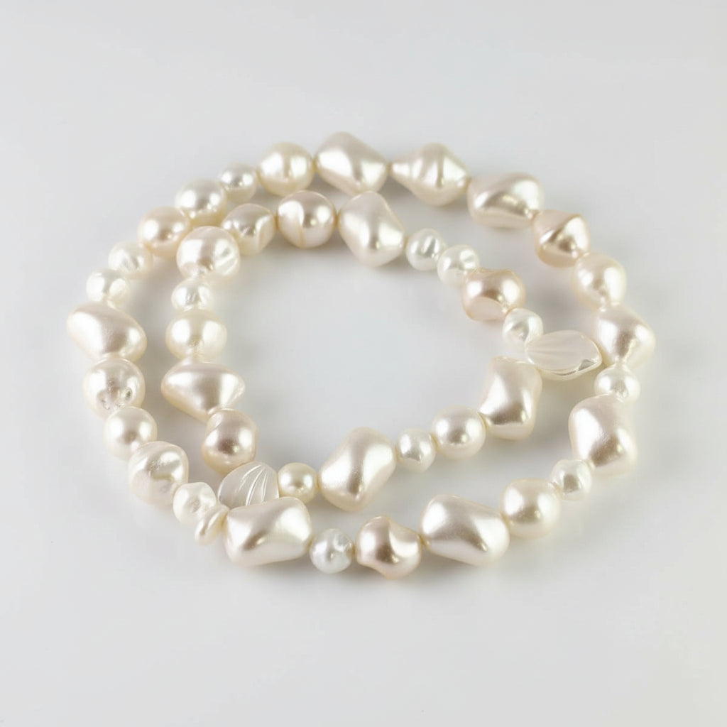 A strand of irregular, baroque-style freshwater pearls in a creamy off-white color, displayed on a white background with a coin for scale.