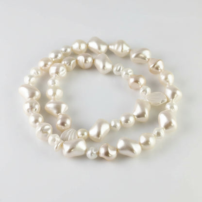 A strand of irregular, baroque-style freshwater pearls in a creamy off-white color, displayed on a white background with a coin for scale.