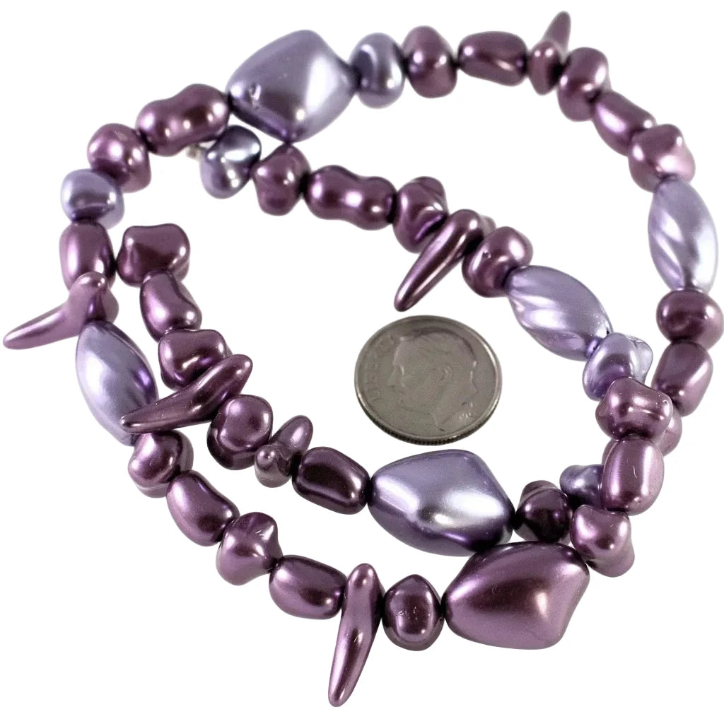 A multi-strand beaded stretch bracelet featuring irregular, glossy purple and lavender beads, shown with a US quarter coin for scale on a white background.