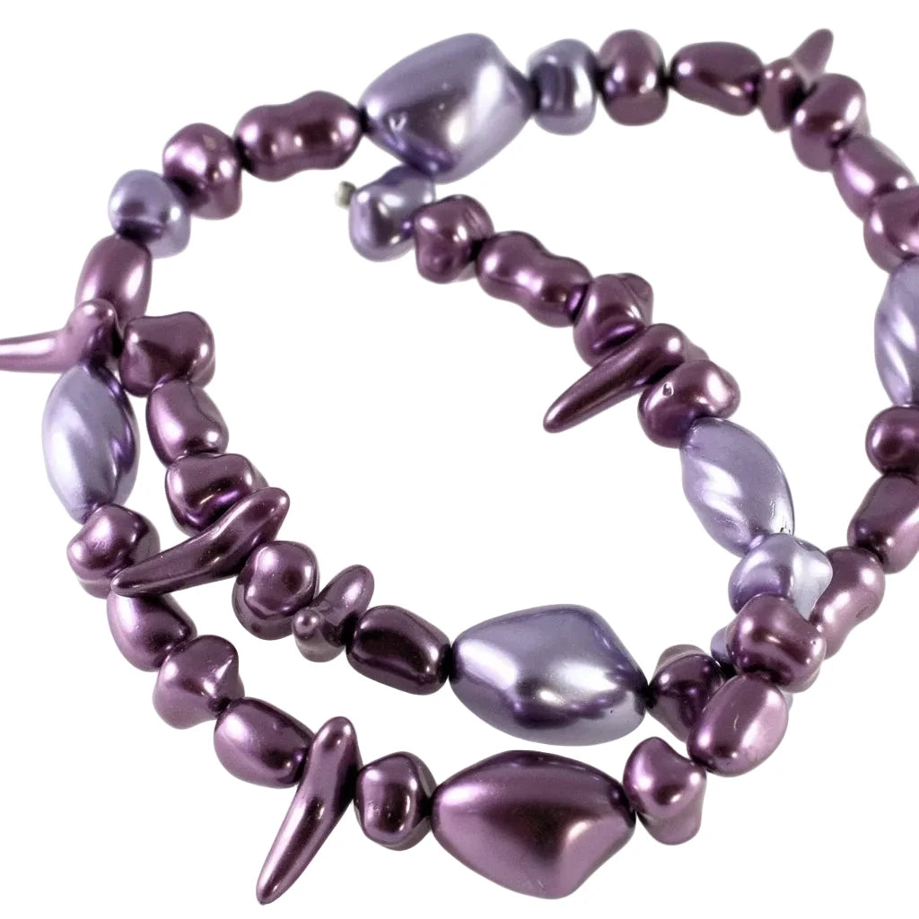 A multi-strand beaded necklace featuring irregular, polished purple and violet beads with a glossy, metallic finish, arranged in a spiral on a plain white background.