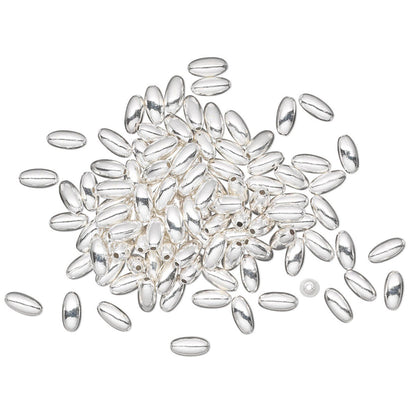 A pile of small, polished silver oval beads with a glossy finish, scattered on a plain white background.