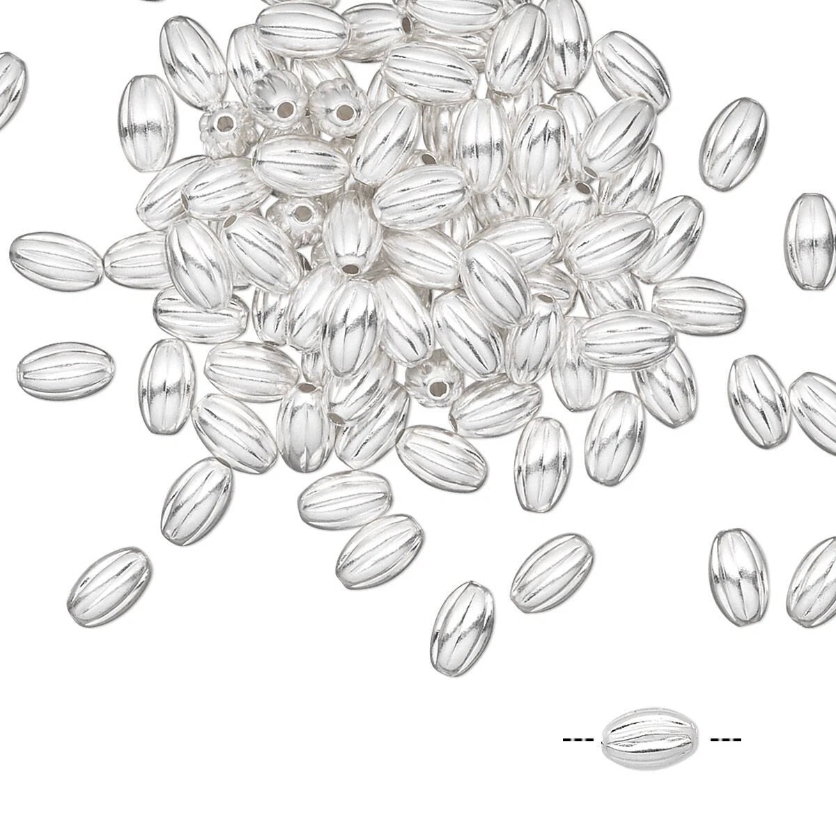 A pile of silver oval beads with a ribbed texture and central holes, scattered on a plain white background with a small detail inset at the bottom right.