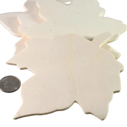 A close-up of several unfinished light wood cutouts shaped like leaves, with a coin placed on the left for scale, on a plain light background.