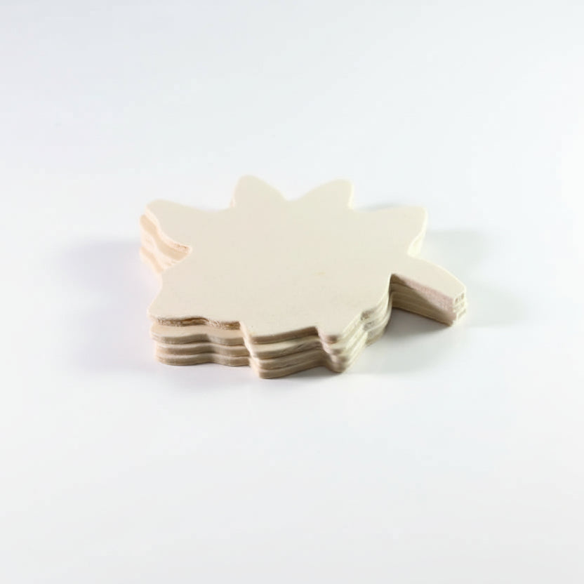 A stack of unpainted, light beige wooden cutouts shaped like a stylized animal or character, shown close-up against a neutral light gray background.