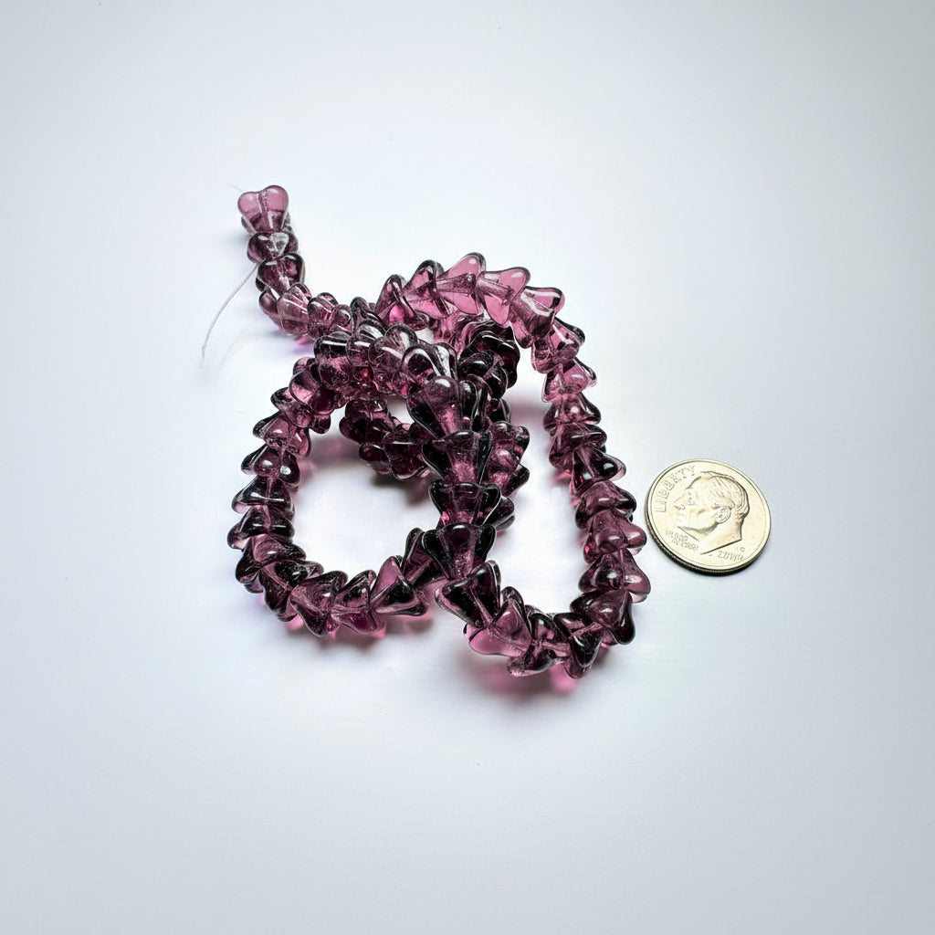 A close-up of a strand of translucent dark purple glass beads, shown next to a US dime for scale on a white background.