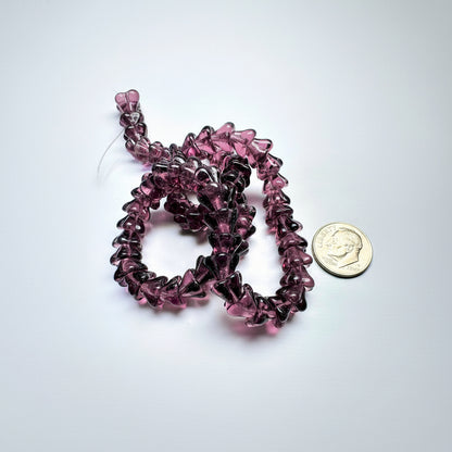 A close-up of a strand of translucent dark purple glass beads, shown next to a US dime for scale on a white background.