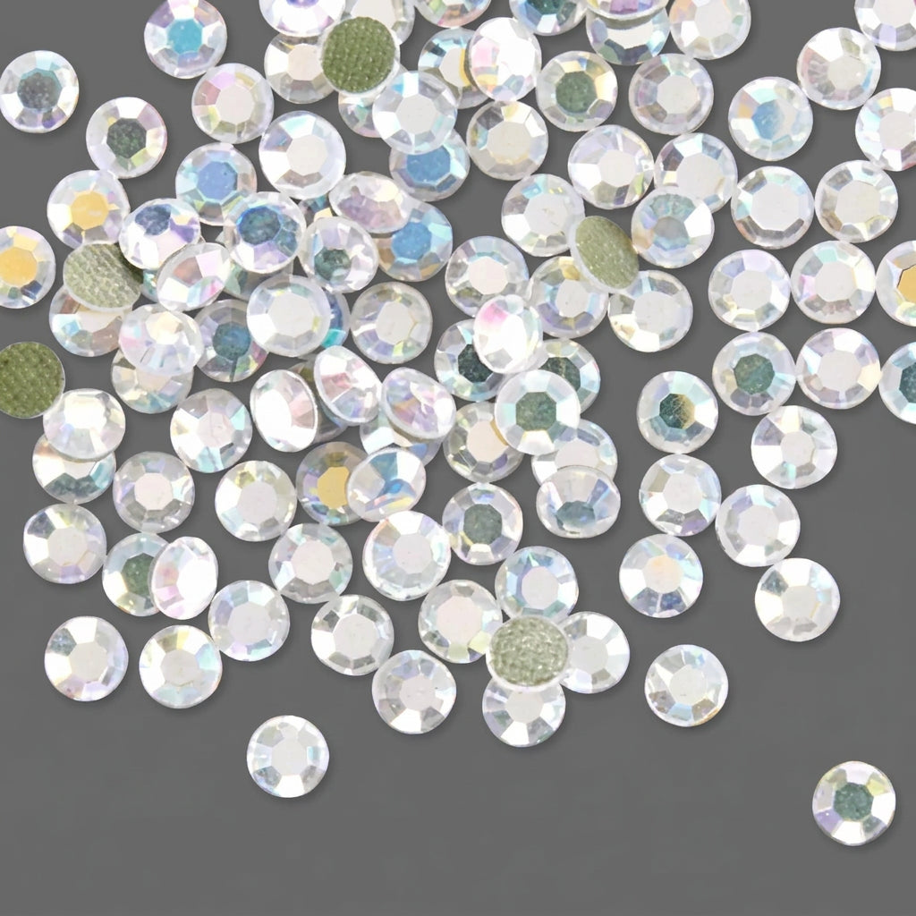 A pile of round, faceted clear rhinestones with an iridescent finish scattered on a solid dark gray background.