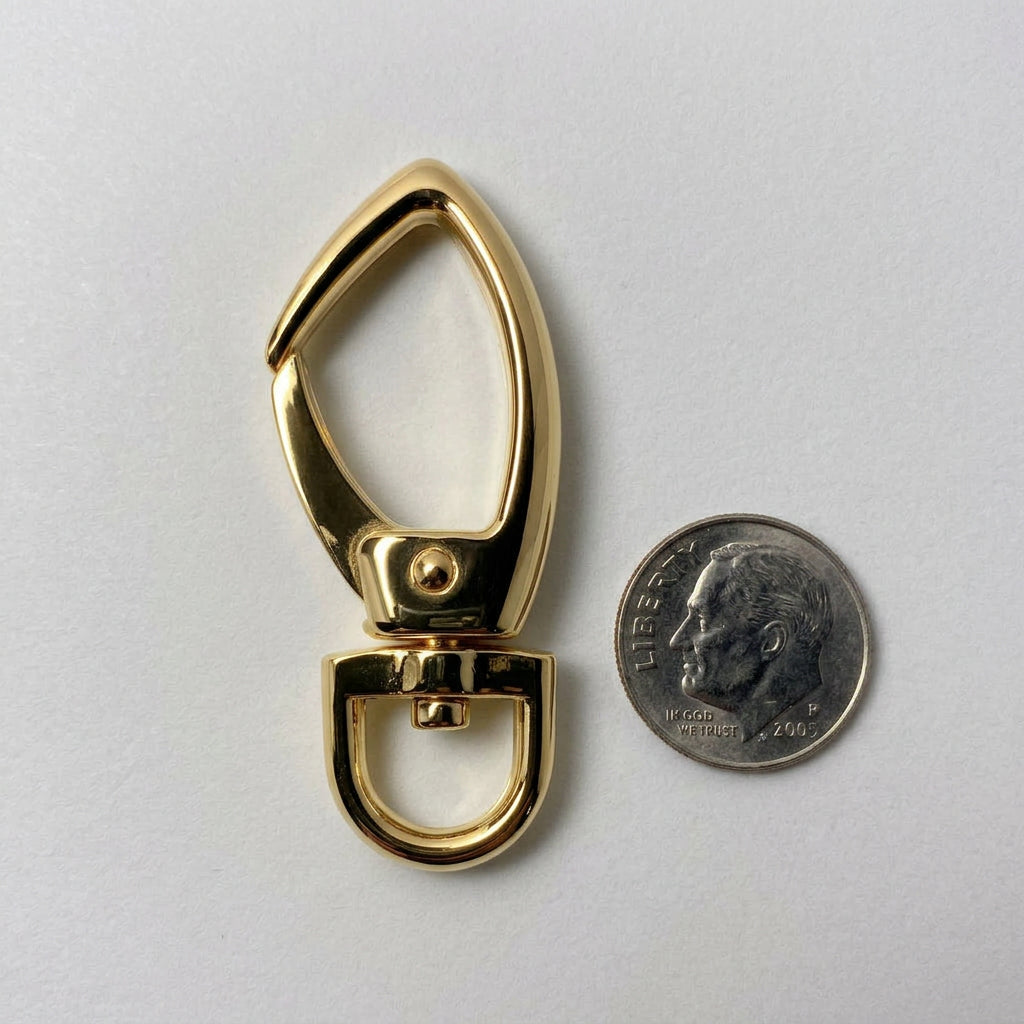 A polished gold metal key ring clasp shown on a light gray background next to a U.S. dime for scale.