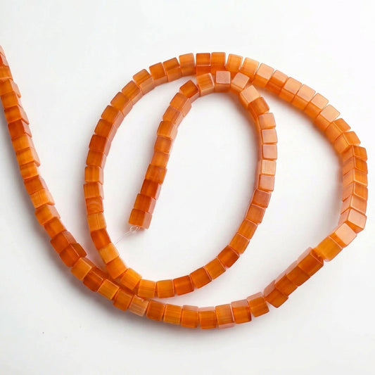 A strand of small, square, translucent orange-red beads arranged in a loose spiral on a plain light gray background.