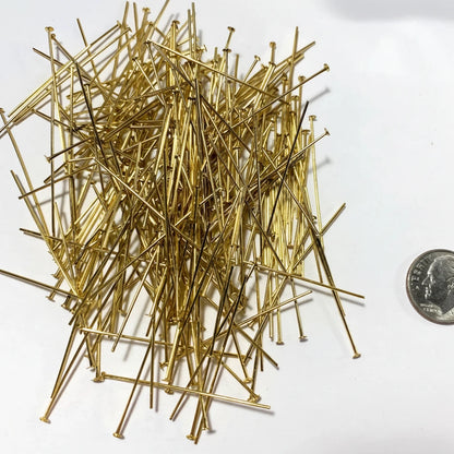 A pile of gold-colored metal push pins on a white background, with a US quarter coin on the right side for scale.