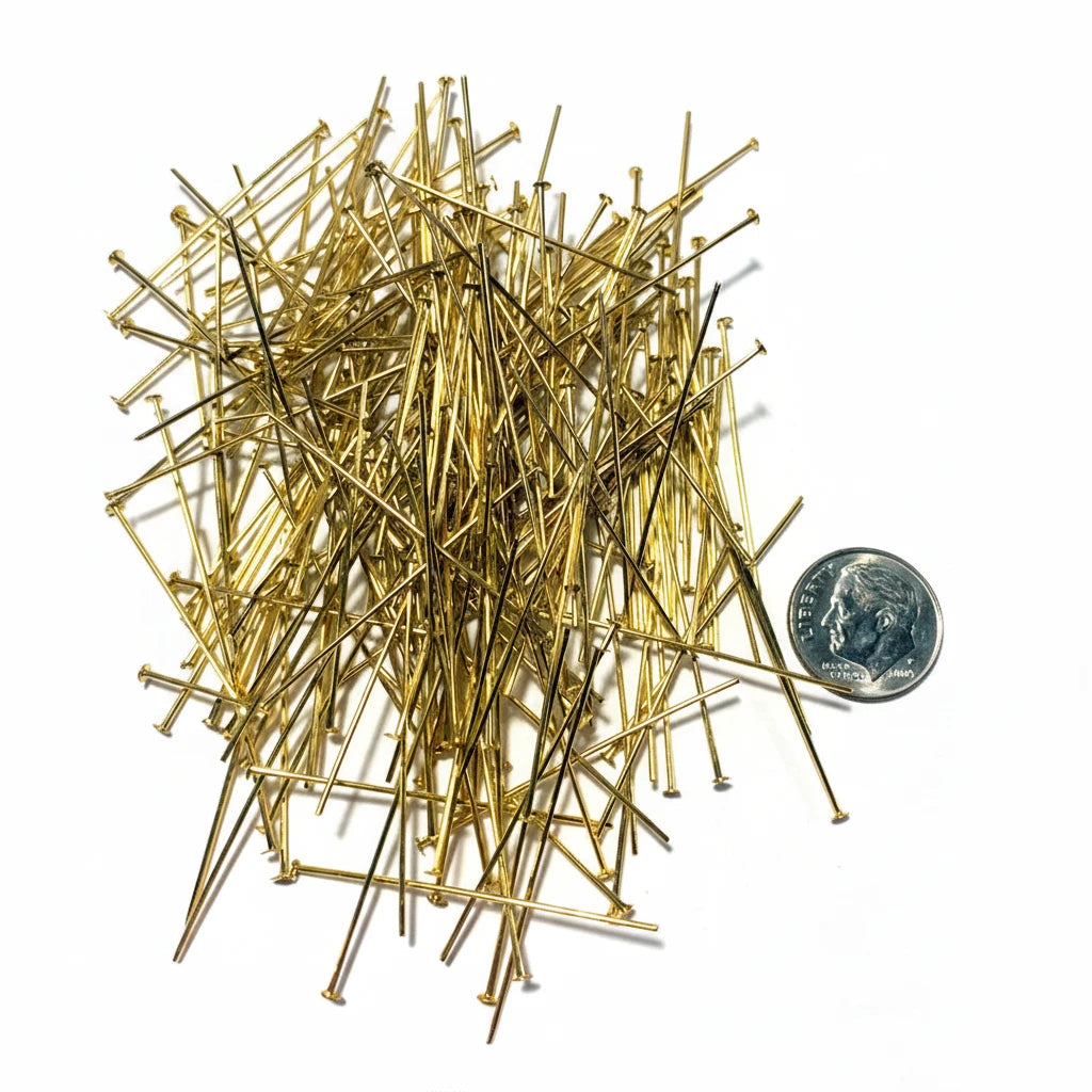 A pile of gold-colored metal craft pins with flat heads, shown on a white background next to a US quarter coin for scale.