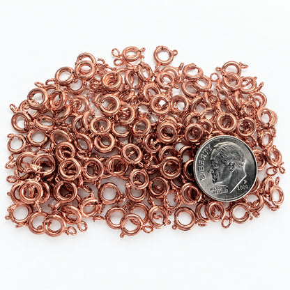 A pile of small copper-toned metal SPRING rings spread across a white surface