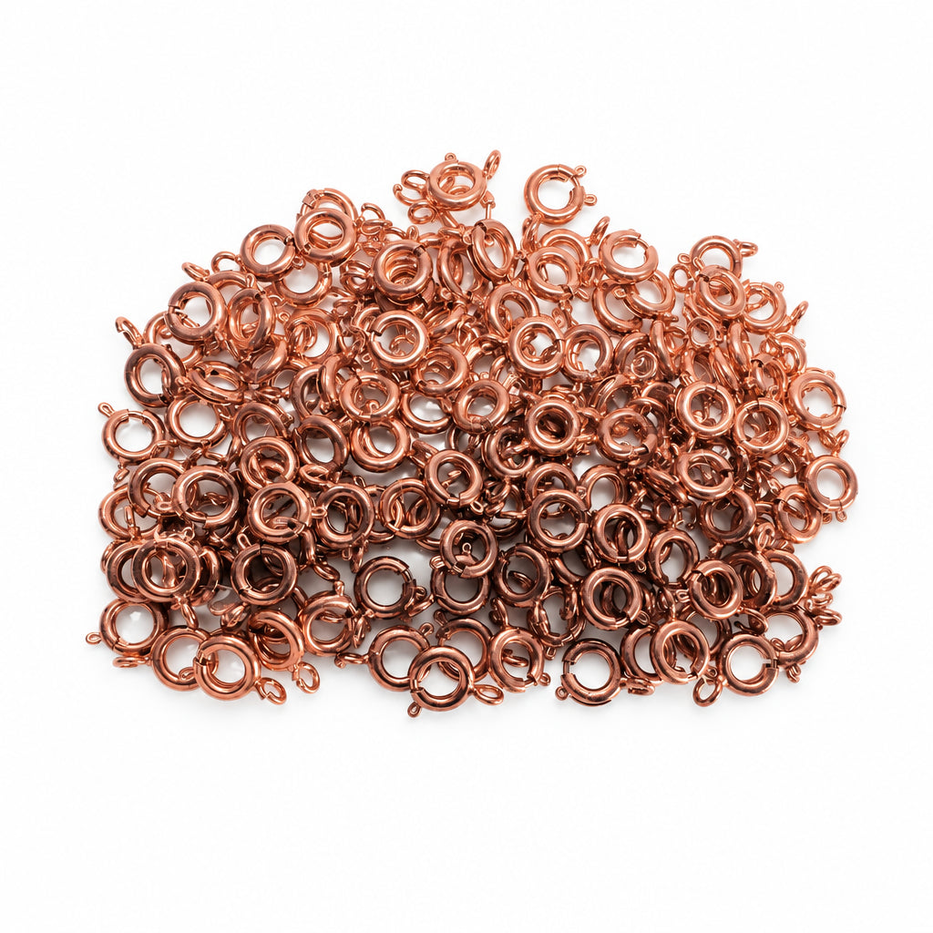 A pile of small copper-colored metal SPRING rings with small loops on each side, photographed close up inside a clear plastic bag.