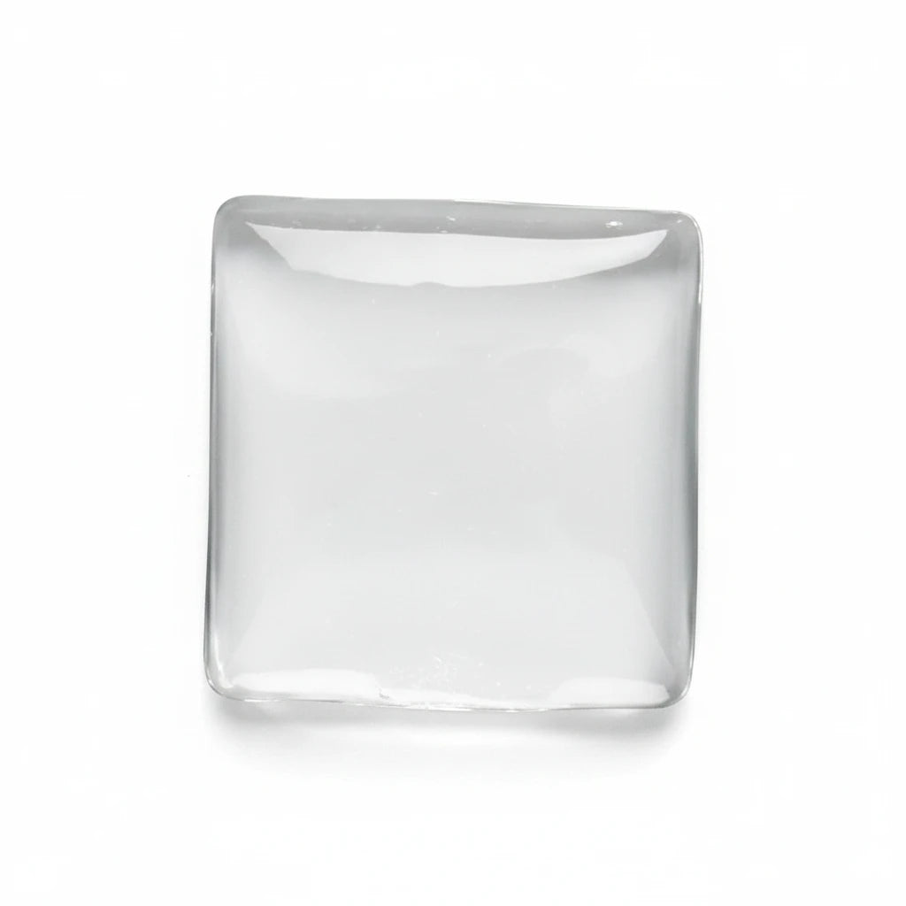 A square, clear glass or acrylic coaster with rounded corners, resting on a smooth, light gray surface.