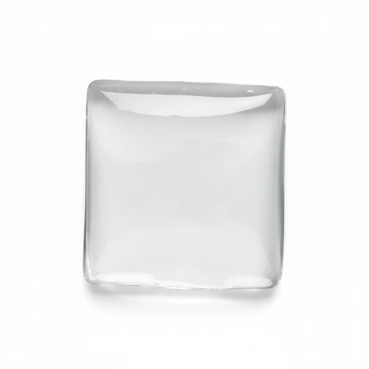 A square, clear glass or acrylic coaster with rounded corners, resting on a smooth, light gray surface.
