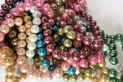 A pile of shiny faux pearl beads in multiple colors, including pink, green, gold, blue, white, and purple, arranged on a light background.