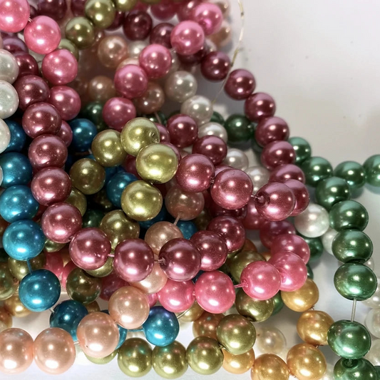 A pile of shiny round pearl beads in multiple colors, including pink, green, gold, blue, white, and peach, arranged on a light background.