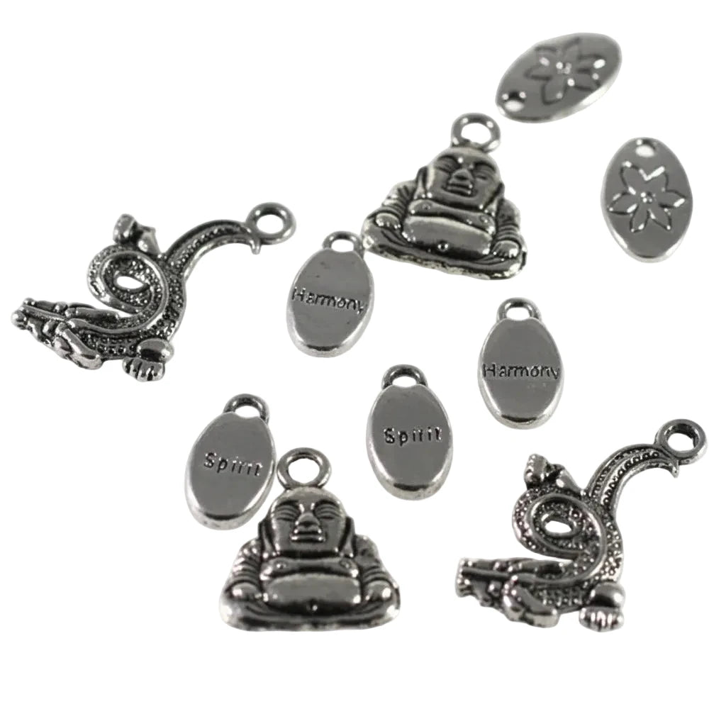A set of silver-toned metal charms and oval tags on a plain white background. The charms include seated Buddha figures, coiled dragon or serpent motifs, and oval tags engraved with the words 'Harmoni' and 'Spiri'.