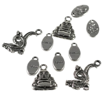 A set of silver-toned metal charms and oval tags on a plain white background. The charms include seated Buddha figures, coiled dragon or serpent motifs, and oval tags engraved with the words 'Harmoni' and 'Spiri'.