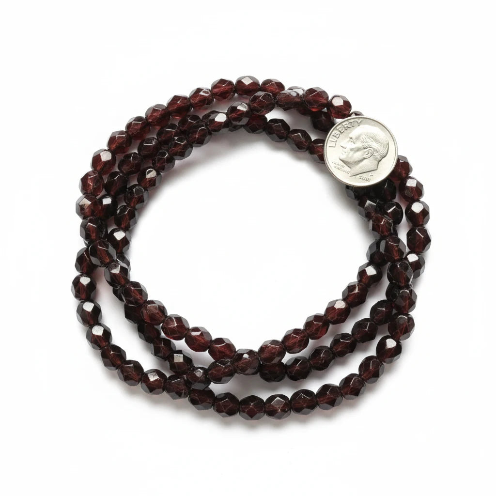 Faceted dark reddish-brown beads arranged in loops on a white background, with a silver coin placed beside them for scale.