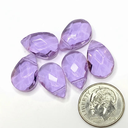 Five faceted teardrop-shaped purple gemstones arranged on a white background, with a U.S. dime in the lower right for scale.