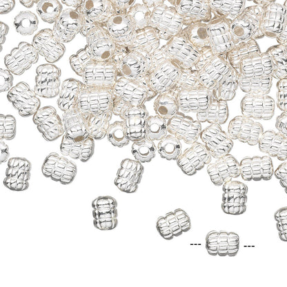 A pile of small silver spacer beads with a textured, ribbed pattern and a central hole, scattered on a plain white background.
