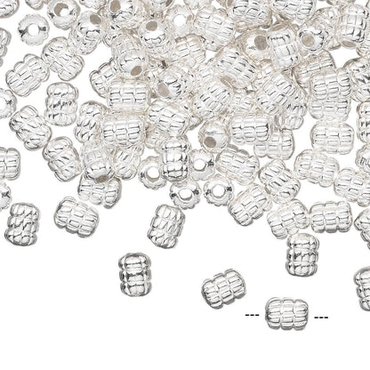 A pile of small silver spacer beads with a textured, ribbed pattern and a central hole, scattered on a plain white background.