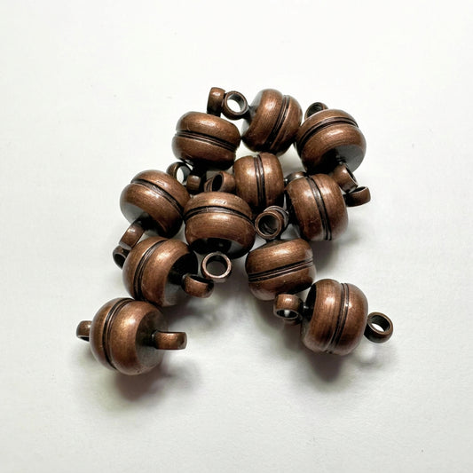 A pile of metallic bronze-colored round spacer beads with loop ends, arranged on a plain light background.