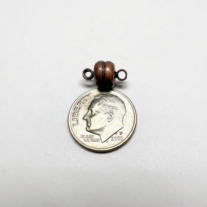 A small ANT COPPER CLASP with two metal loops on top, shown resting on a silver dime for scale against a light gray background.