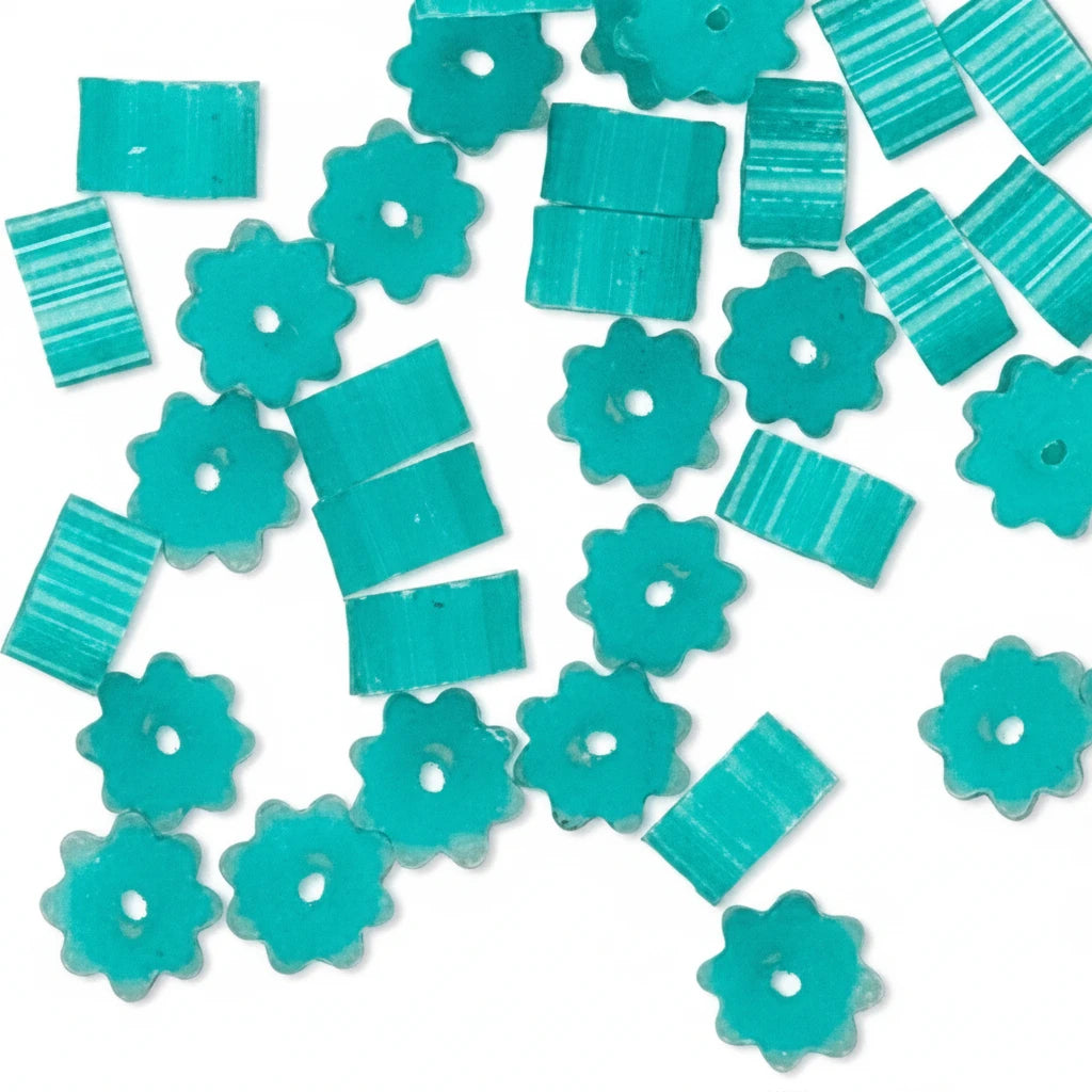 Turquoise craft beads in flower and striped square shapes scattered on a white background.